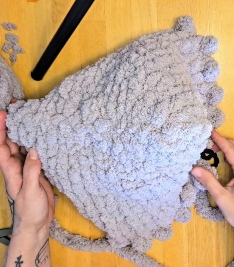 Puede incluir: Un gorro de punto de color gris con una superficie texturizada y un pomp&oacute;n en la parte superior.