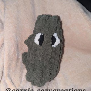 May include: A handmade, plush, gray creature with white and black eyes. The creature is made of a soft, textured material. The Etsy shop name "@carrie_cozycreations" is visible at the bottom of the image.