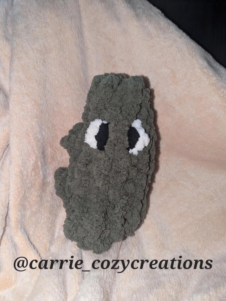May include: A handmade, plush, gray creature with white and black eyes. The creature is made of a soft, textured material. The Etsy shop name "@carrie_cozycreations" is visible at the bottom of the image.
