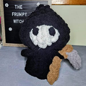 May include: A handmade black plush Grim Reaper doll with a white skull face and a brown and gray scythe. The doll is next to a framed letter board that reads "THE FRUMPY WITCH".