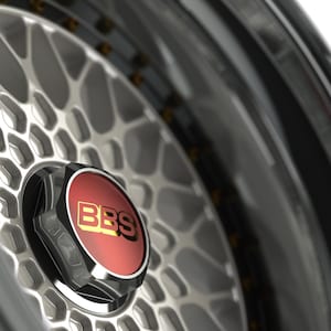 Könnte beinhalten: Nahaufnahme einer Autoradfelge mit silbernem und schwarzem Finish. Die Radkappe ist rot mit den goldenen Buchstaben "BBS". Die Felge hat ein komplexes geometrisches Muster.