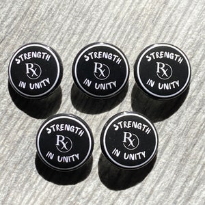 May include: Five black and white round buttons with the text "STRENGTH IN UNITY" and a stylized "Rx" symbol in the center.