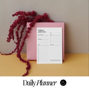 Könnte beinhalten: Ein weißer Tagesplaner mit dem Text "Today is a GREAT DAY." oben. Der Planer hat Abschnitte für tägliche Affirmationen, Zeitplan, To-Do-Liste und kreativen Raum. Der Planer liegt auf einer rosa Oberfläche.