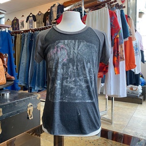 Puede incluir: Una camiseta gris y negra con un estampado gráfico descolorido. La camiseta tiene un diseño de manga raglan con mangas grises y un cuerpo negro.