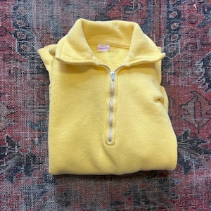 Puede incluir: Un suéter de vellón amarillo con cremallera blanca. El suéter tiene un cuello alto y una pequeña etiqueta roja con el texto "Russell" en ella.