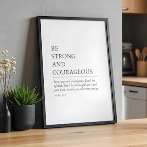 May include: Black framed print with the text "BE STRONG AND COURAGEOUS" and a quote from Joshua 1:9. The print is hanging on a gray wall in a kitchen.