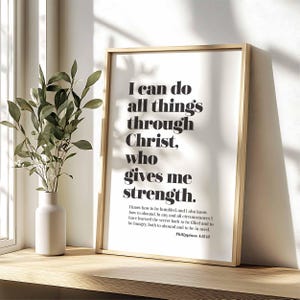 May include: A black and white inspirational quote print with a wooden frame. The quote reads "I can do all things through Christ, who gives me strength." The quote is from Philippians 4:12-13.