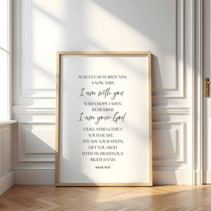 May include: A framed print with a light wood frame. The print features elegant script with the text "When fear surrounds, know this, I am with you...I am your God." The print is displayed on a wooden floor.