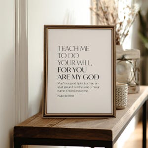 Könnte beinhalten: Gerahmter Druck mit dem Text "TEACH ME TO DO YOUR WILL, FOR YOU ARE MY GOD" in minimalistischem Stil. Der Druck enthält ein Zitat aus Psalm 143:10-11. Der Rahmen ist braun und der Druck wird auf einer Holzoberfläche angezeigt.