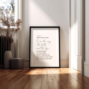May include: A framed print with a black border, featuring the text "I am the way, the truth, and the life." The print is displayed on a wooden floor, with a neutral-toned background. Decorative elements include dried plants in a vase.