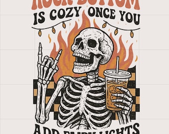 May include: Illustration of a skeleton with a drink, flames, and fairy lights. Text reads "Rock Bottom is Cozy Once You Add Fairy Lights." The skeleton is giving a rock and roll hand gesture.