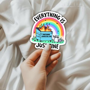 K&ouml;nnte beinhalten: Ein Aufkleber mit einem Regenbogen und einem brennenden M&uuml;lleimer. Der Text lautet "Alles ist gut" und "Emotionales M&uuml;lltonnenfeuer". Ein Waschb&auml;r steht neben dem M&uuml;lleimer.