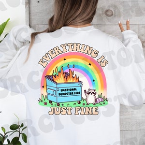 K&ouml;nnte beinhalten: Wei&szlig;es Sweatshirt mit einem Regenbogen und einem blauen M&uuml;llcontainer in Flammen mit dem Text "Alles ist gut" und einem Waschb&auml;ren mit einem Peace-Zeichen.