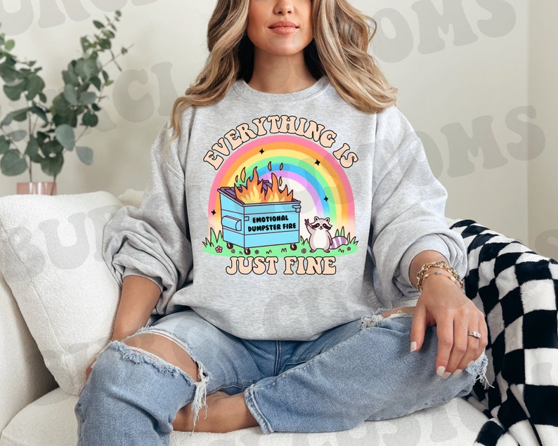K&ouml;nnte beinhalten: Ein graues Sweatshirt mit dem Text "Everything is just fine" und einem Cartoon-Bild eines Waschb&auml;ren, der neben einem M&uuml;lltonnenfeuer steht, mit dem Text "Emotional Dumpster Fire".