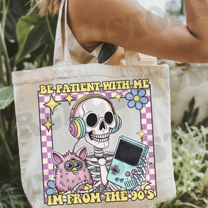 May include: A white tote bag with a pink, blue, and yellow graphic of a skeleton wearing headphones and holding a video game. The text on the bag reads "Be patient with me, I'm from the 90's".