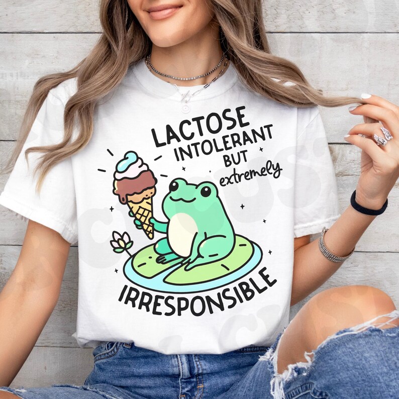 Puede incluir: Camiseta blanca con una rana verde sosteniendo un cono de helado. El texto en la camiseta dice "Lactose Intolerant But Extremely Irresponsible".