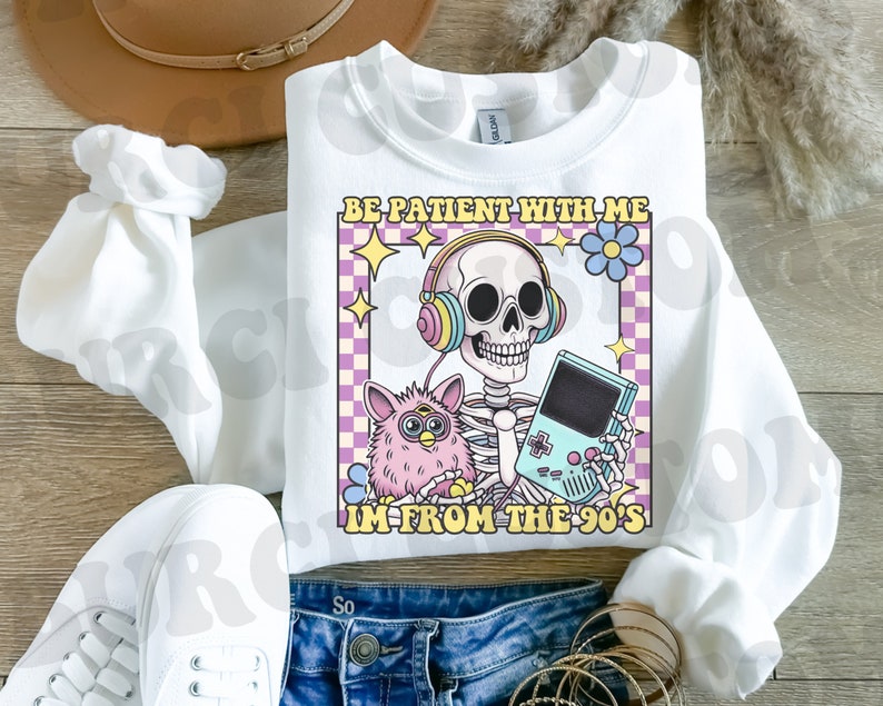May include: White sweatshirt with a graphic of a skeleton wearing headphones and holding a video game controller. The graphic also includes a pink fuzzy toy and the text "Be patient with me I'm from the 90's".