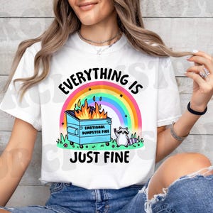 K&ouml;nnte beinhalten: Wei&szlig;es T-Shirt mit einem Regenbogen, einem M&uuml;lltonnenfeuer und einem Waschb&auml;ren. Der Text auf dem Shirt lautet "Alles ist gut."