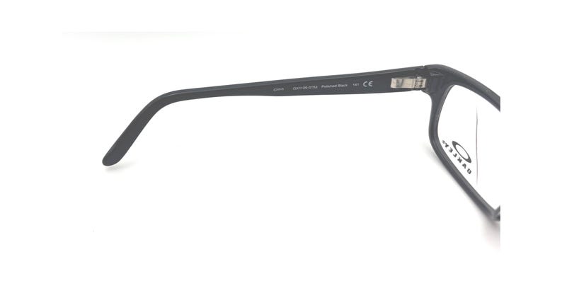 Puede incluir: Gafas negras con montura rectangular y patillas curvas. La patilla tiene el texto "OAKLEY" y otras marcas. Las lentes transparentes est&aacute;n dentro de la montura. Sobre un fondo blanco.