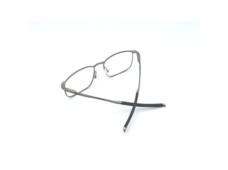 May include: A pair of silver-toned spectacles with black temple tips. The glasses are folded in half and the temple tips are crossed.