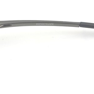 May include: A pair of rimless eyeglasses with a dark gray metal frame. The temples curve gently, and the text "BOTTEGA VENETA" is visible on the temple. The glasses are set against a white background.