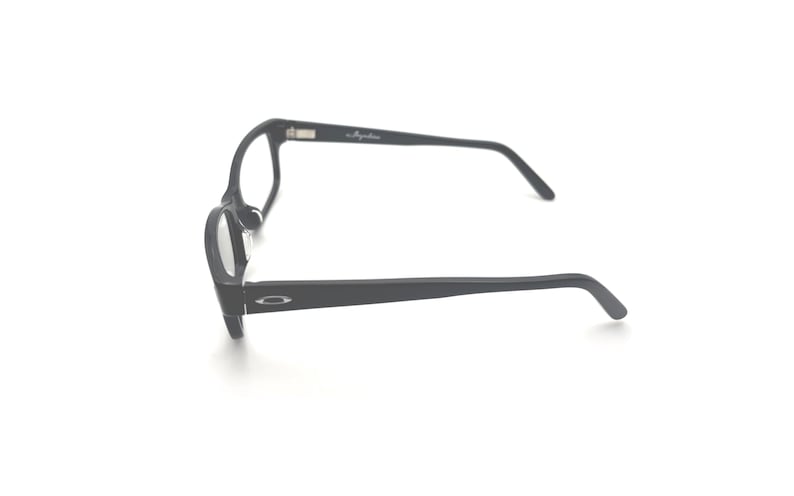 Puede incluir: Gafas negras con montura rectangular redondeada. Las gafas tienen un acabado mate y un logotipo sutil en la patilla. Las lentes son transparentes. El dise&ntilde;o general es moderno y minimalista.