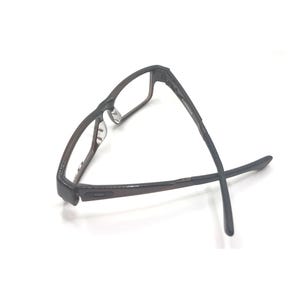 May include: Dark brown rectangular eyeglasses with a textured frame. The glasses have clear lenses and a classic design, suitable for everyday wear. The temples are thin and extend outwards.