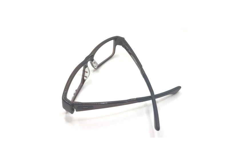 May include: Dark brown rectangular eyeglasses with a textured frame. The glasses have clear lenses and a classic design, suitable for everyday wear. The temples are thin and extend outwards.