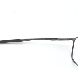 May include: A pair of grey metal spectacles with clear lenses. The glasses have a thin, black temple arm and a small, clear nose pad.