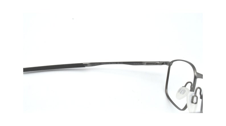 May include: A pair of grey metal spectacles with clear lenses. The glasses have a thin, black temple arm and a small, clear nose pad.