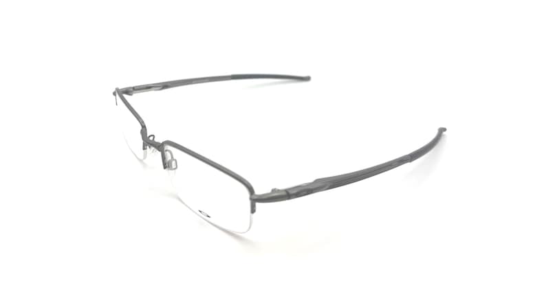 May include: Rimless eyeglasses with a dark gray metal frame. The lenses are clear, and the temples curve gently. The glasses are set against a white background, highlighting their minimalist design.