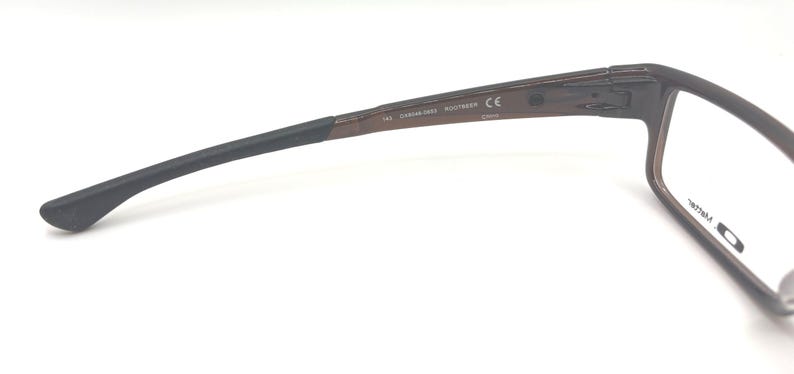 May include: Brown rectangular eyeglasses with black temples. The glasses have a sleek, modern design. The temple arm has the text "CE" and other markings. The glasses are designed for vision correction.