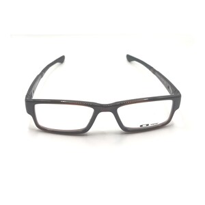 May include: Rectangular eyeglasses with a dark gray frame and brown accents. The lenses are clear, and the temples are thin and angled. The brand logo is visible on the lower right lens.