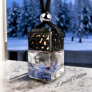 May include: A black car air freshener with a clear glass bottle containing blue and white crystals. The bottle has a black metal frame with a decorative design. The label on the bottle reads "Innergy Winter's Eve Limited Edition".