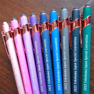 May include: A selection of pens in various colours, each featuring rose gold detailing. The pens, in shades like pink, purple, and blue, have the text "2025 Yokohama Japan Special Convention" printed on them. The pens are arranged in a row.