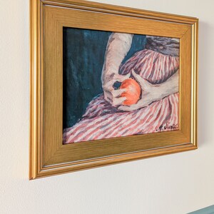 Painting of a woman holding fruit in a gold frame on a white wall