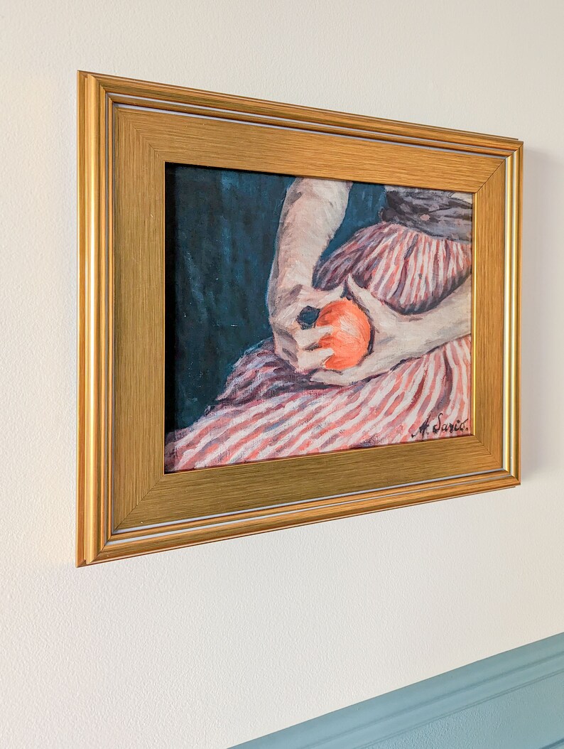 Painting of a woman holding fruit in a gold frame on a white wall