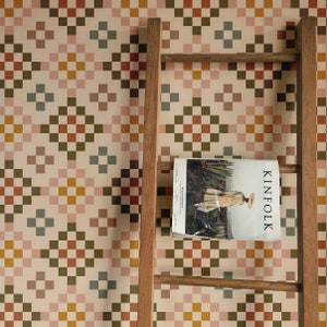 May include: A wooden ladder leaning against a wall covered in a patterned wallpaper with squares of pink, red, yellow, green, and brown. A magazine titled "Kinfolk" is resting on the ladder.