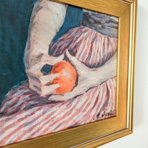 Painting of a woman holding fruit in a gold frame on a white wall