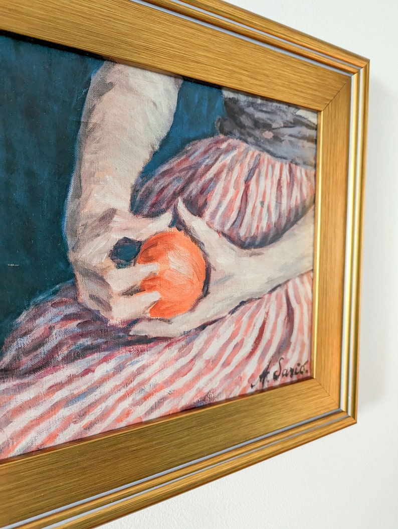 Painting of a woman holding fruit in a gold frame on a white wall