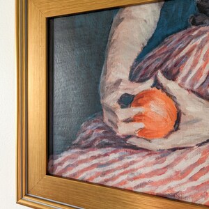 Painting of a woman holding fruit in a gold frame on a white wall