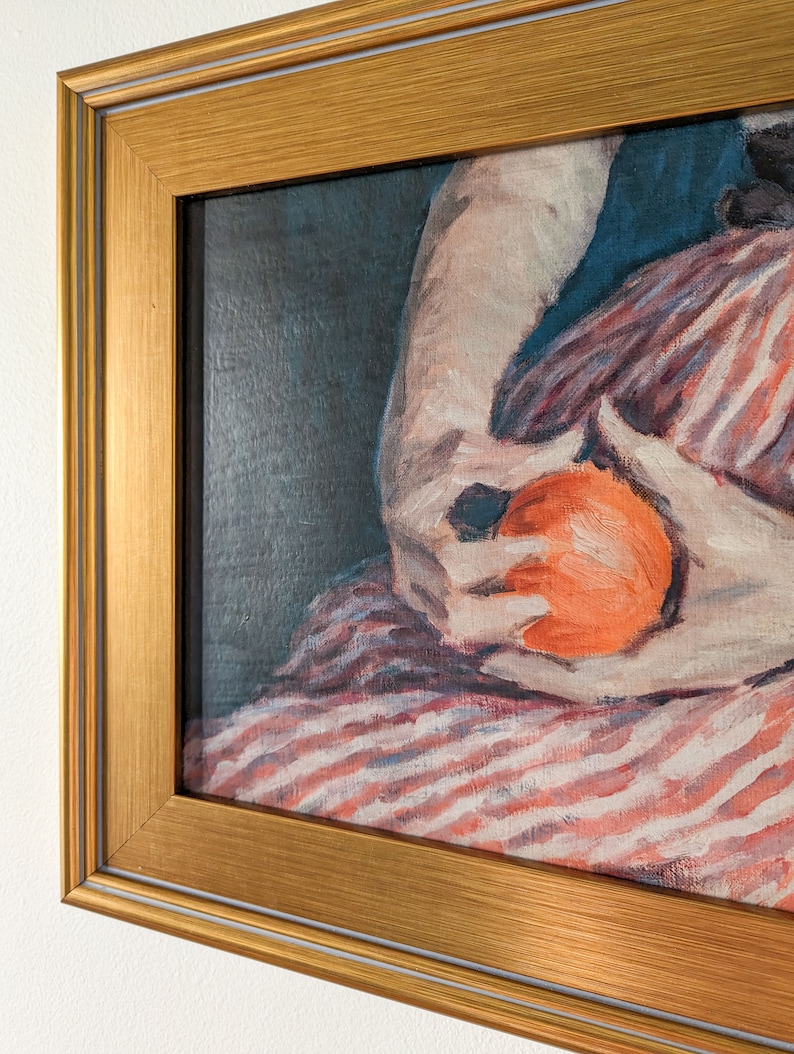 Painting of a woman holding fruit in a gold frame on a white wall