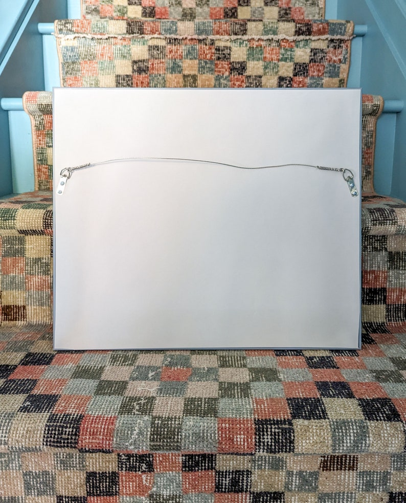 The back of a framed work of art on a stair with checkered vintage runner.