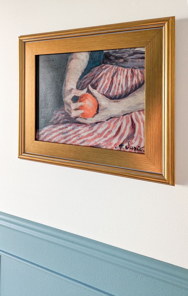Painting of a woman holding fruit in a gold frame on a white wall