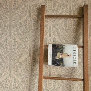 May include: A wooden ladder leaning against a wall with a beige wallpaper featuring a repeating pattern of green leafy branches. A magazine titled "Kinfolk" is resting on the ladder.