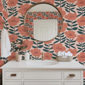 May include: A bathroom with a white vanity, a round gold mirror, and floral wallpaper. The wallpaper features large coral-colored flowers with dark green leaves on a light pink background. A white towel hangs on a gold towel rack.