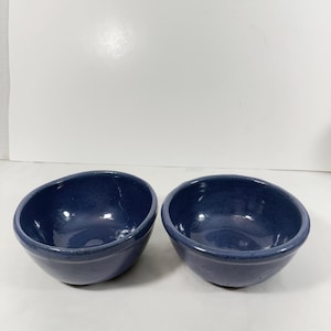 May include: Two navy blue ceramic bowls with a speckled finish. The bowls have a rounded shape with a slightly angled rim. They are set against a white background.