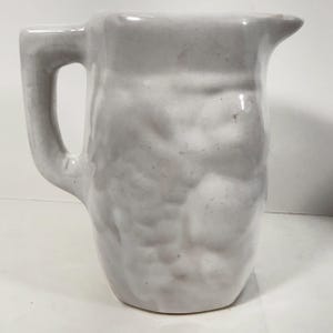 May include: A white ceramic pitcher with a handle and a spout. The pitcher has a textured surface and a slightly irregular shape, suggesting it may be handmade. The pitcher is suitable for serving beverages.