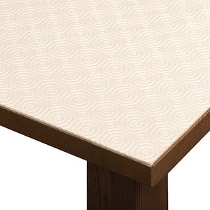 May include: A close-up of a white table protector with a hexagonal pattern. The protector is placed on a dark brown wooden table.