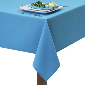 May include: A bright blue tablecloth with a white rose and green leaves on a white plate. The tablecloth is made of a smooth, wrinkle-resistant fabric.